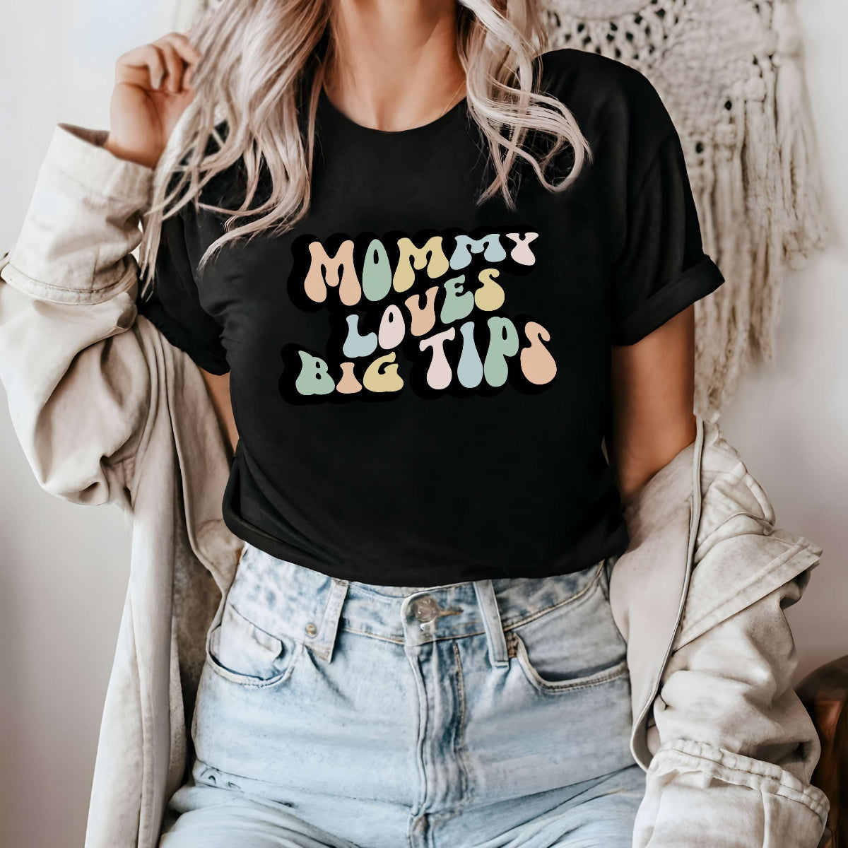 Graphic tee for women. The color of the shirt is black. In a colorful, typically 70s retro-style font it says Mommy Loves Big Tips.