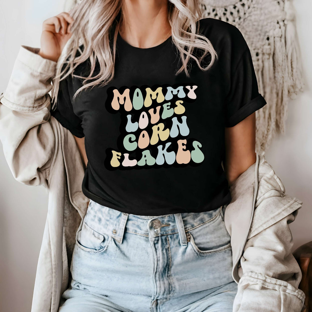 Graphic tee for women. The color of the shirt is black. In a colorful, typically 70s retro-style font it says Mommy Loves Corn Flakes.