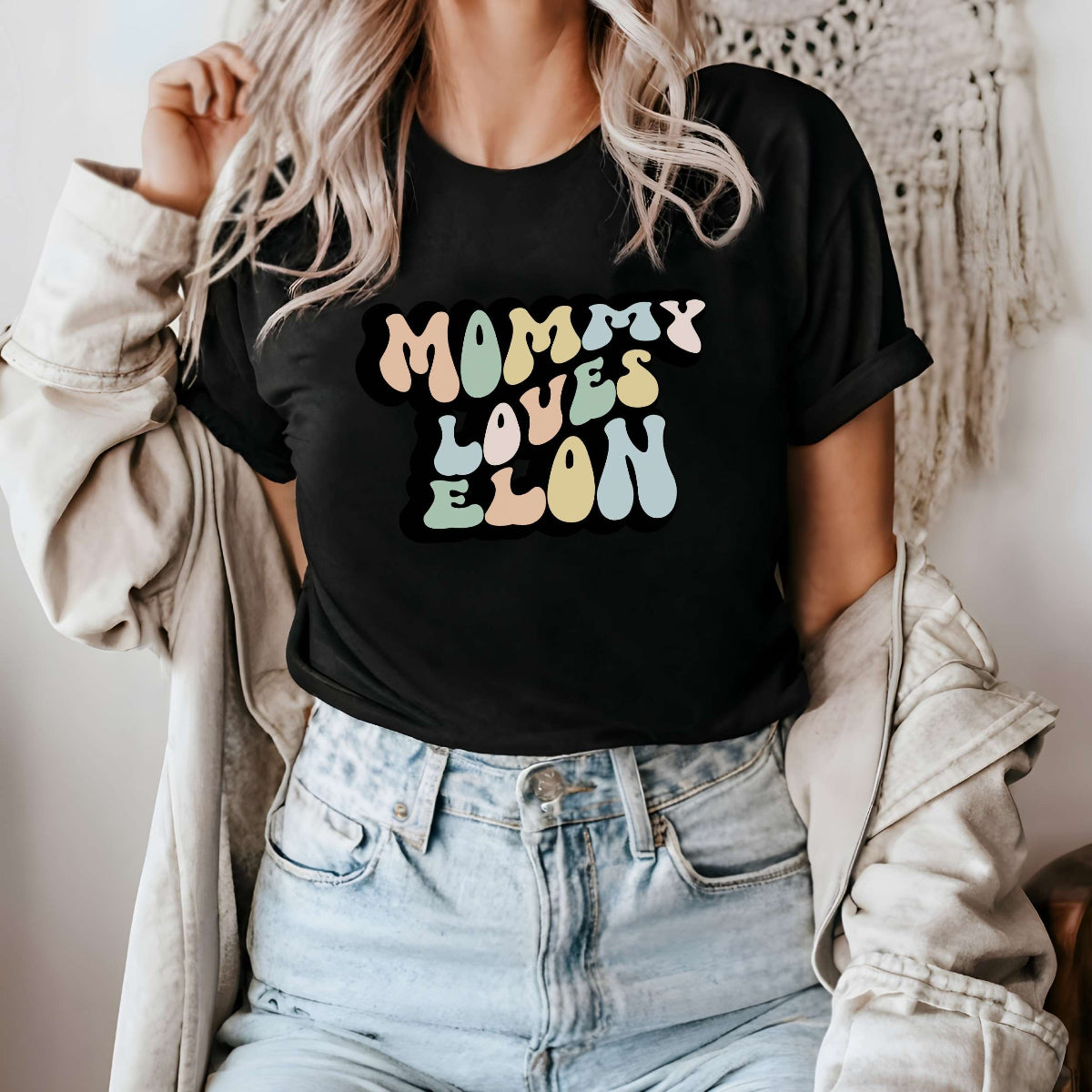 Graphic tee for women. The color of the shirt is black. In a colorful, typically 70s retro-style font it says Mommy Loves Elon.