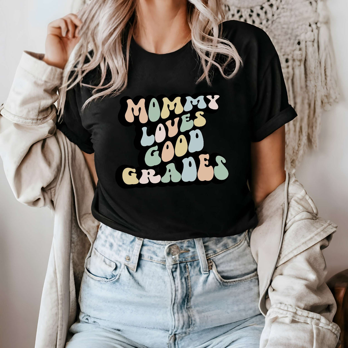 Graphic tee for women. The color of the shirt is black. In a colorful, typically 70s retro-style font it says Mommy Loves Good Grades.
