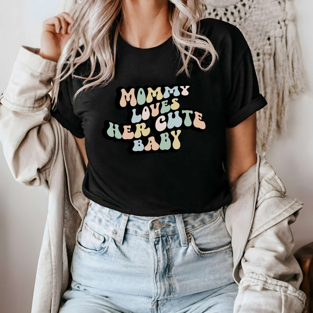 Graphic tee for women. The color of the shirt is black. In a colorful, typically 70s retro-style font it says Mommy Loves Her Cute Baby.