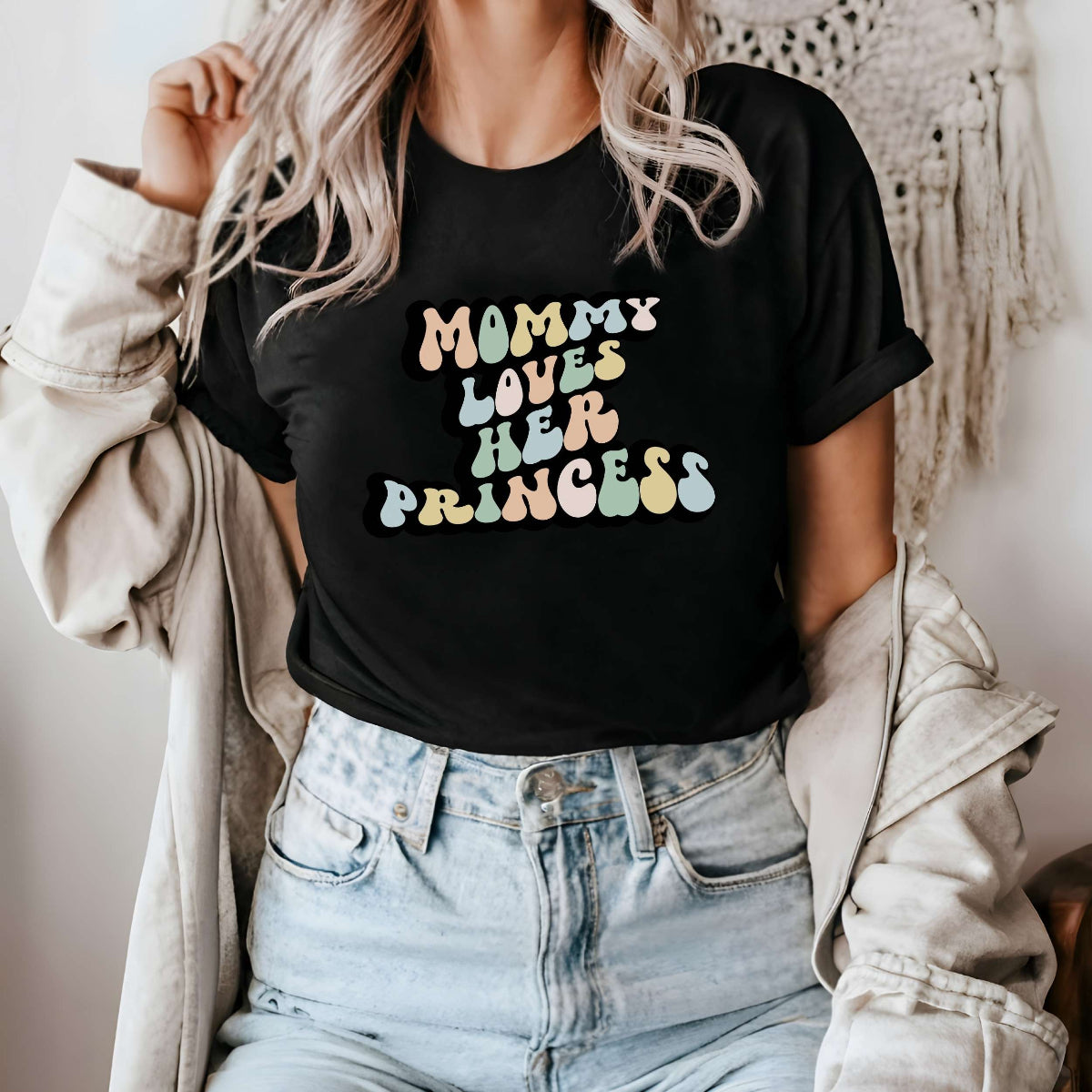 Graphic tee for women. The color of the shirt is black. In a colorful, typically 70s retro-style font it says Mommy Loves Her Princess.