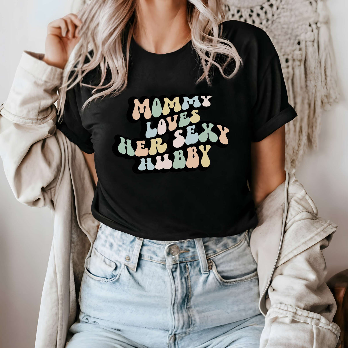 Graphic tee for women. The color of the shirt is black. In a colorful, typically 70s retro-style font it says Mommy Loves Her Sexy Hubby.