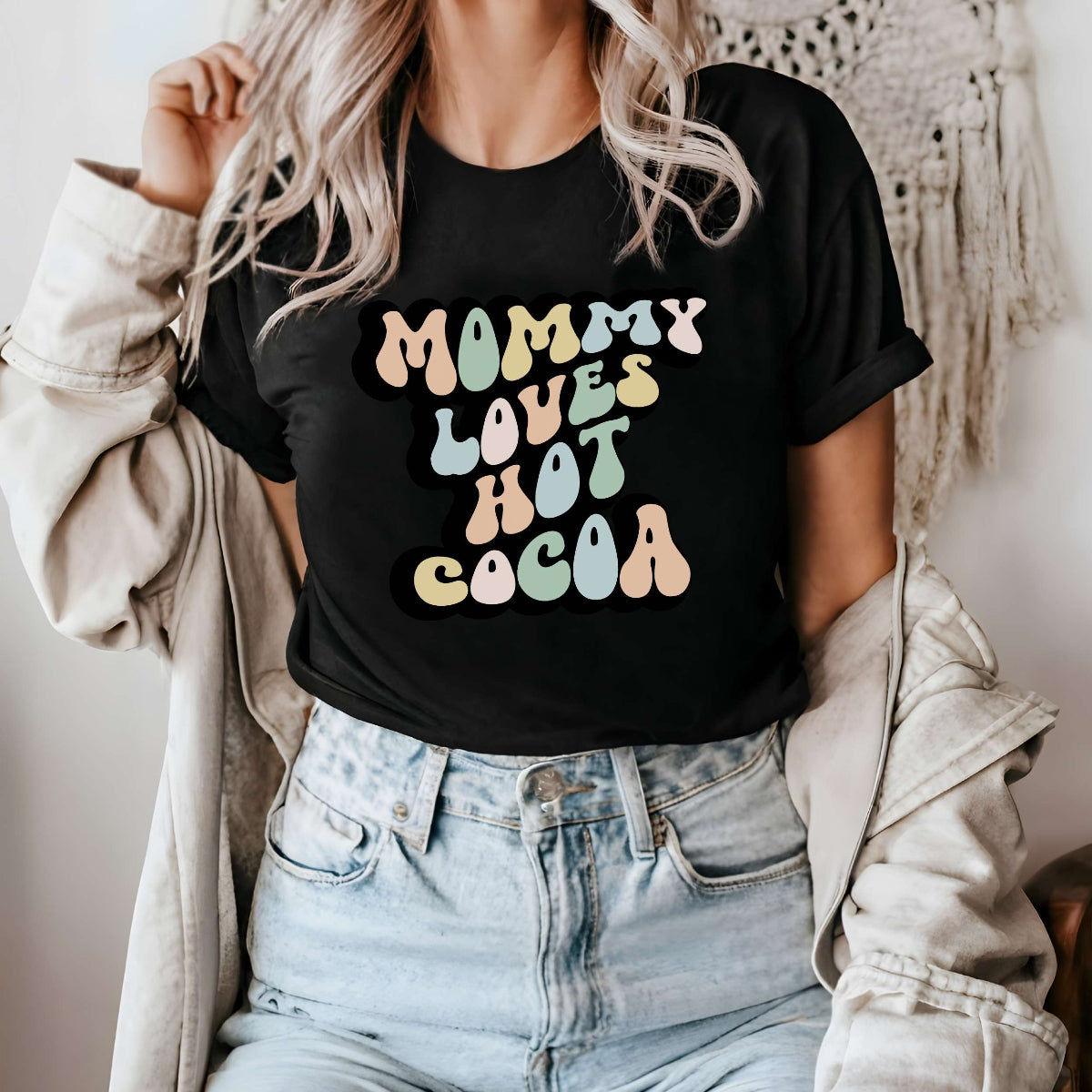 Graphic tee for women. The color of the shirt is black. In a colorful, typically 70s retro-style font it says Mommy Loves Hot Cocoa.