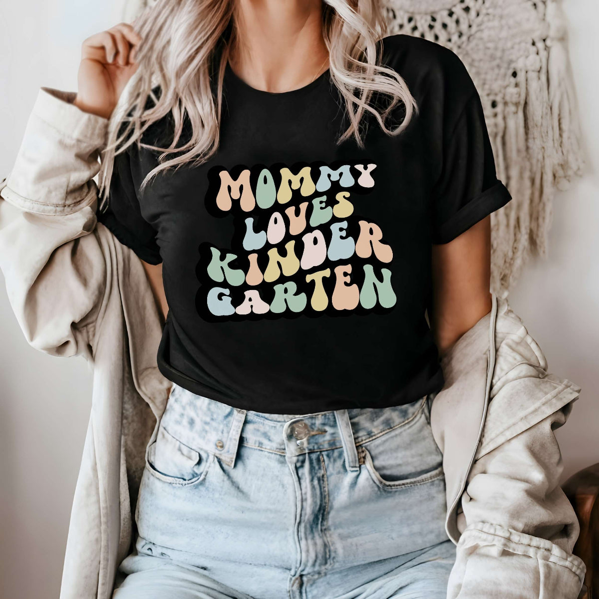 Graphic tee for women. The color of the shirt is black. In a colorful, typically 70s retro-style font it says Mommy Loves Kindergarten.