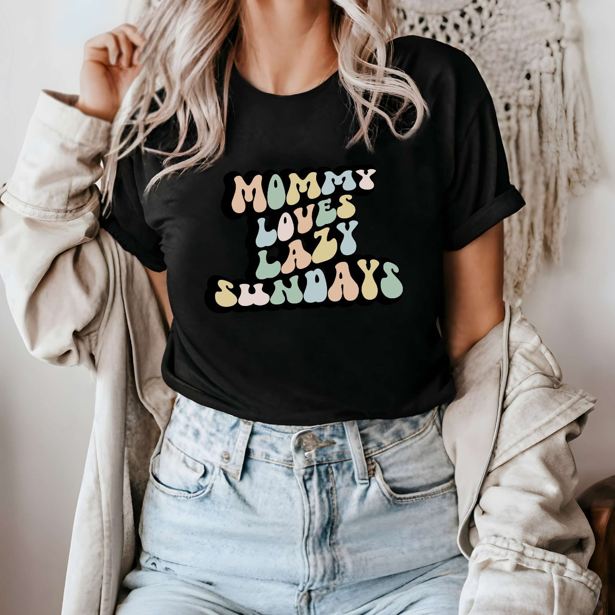 Graphic tee for women. The color of the shirt is black. In a colorful, typically 70s retro-style font it says Mommy Loves Lazy Sundays.