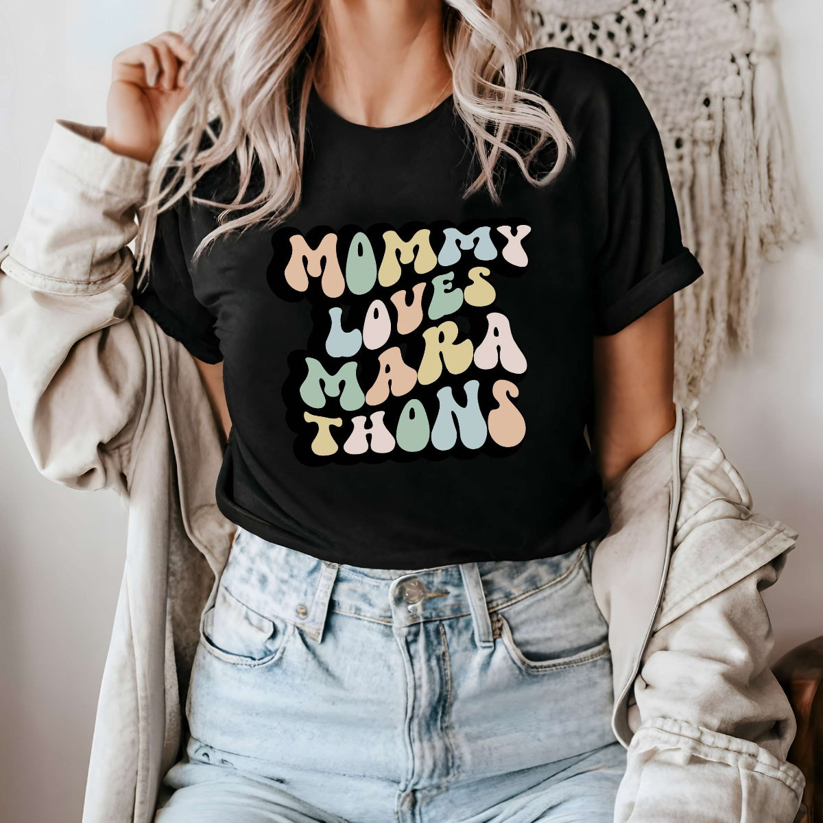 Graphic tee for women. The color of the shirt is black. In a colorful, typically 70s retro-style font it says Mommy Loves Marathons.