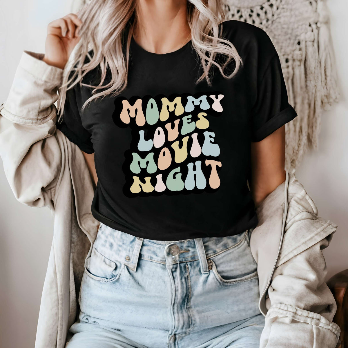 Graphic tee for women. The color of the shirt is black. In a colorful, typically 70s retro-style font it says Mommy Loves Movie Night.