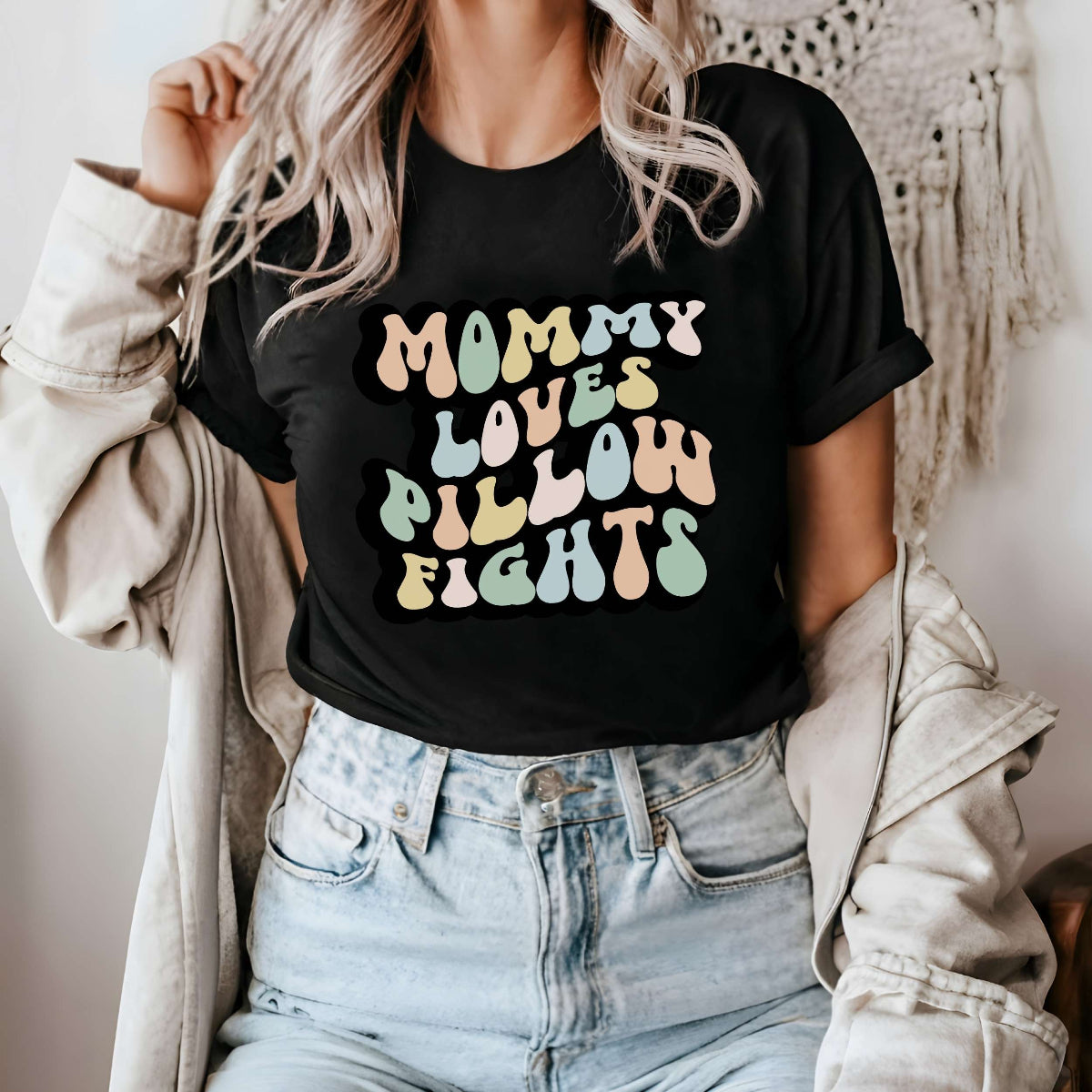 Graphic tee for women. The color of the shirt is black. In a colorful, typically 70s retro-style font it says Mommy Loves Pillow Fights.