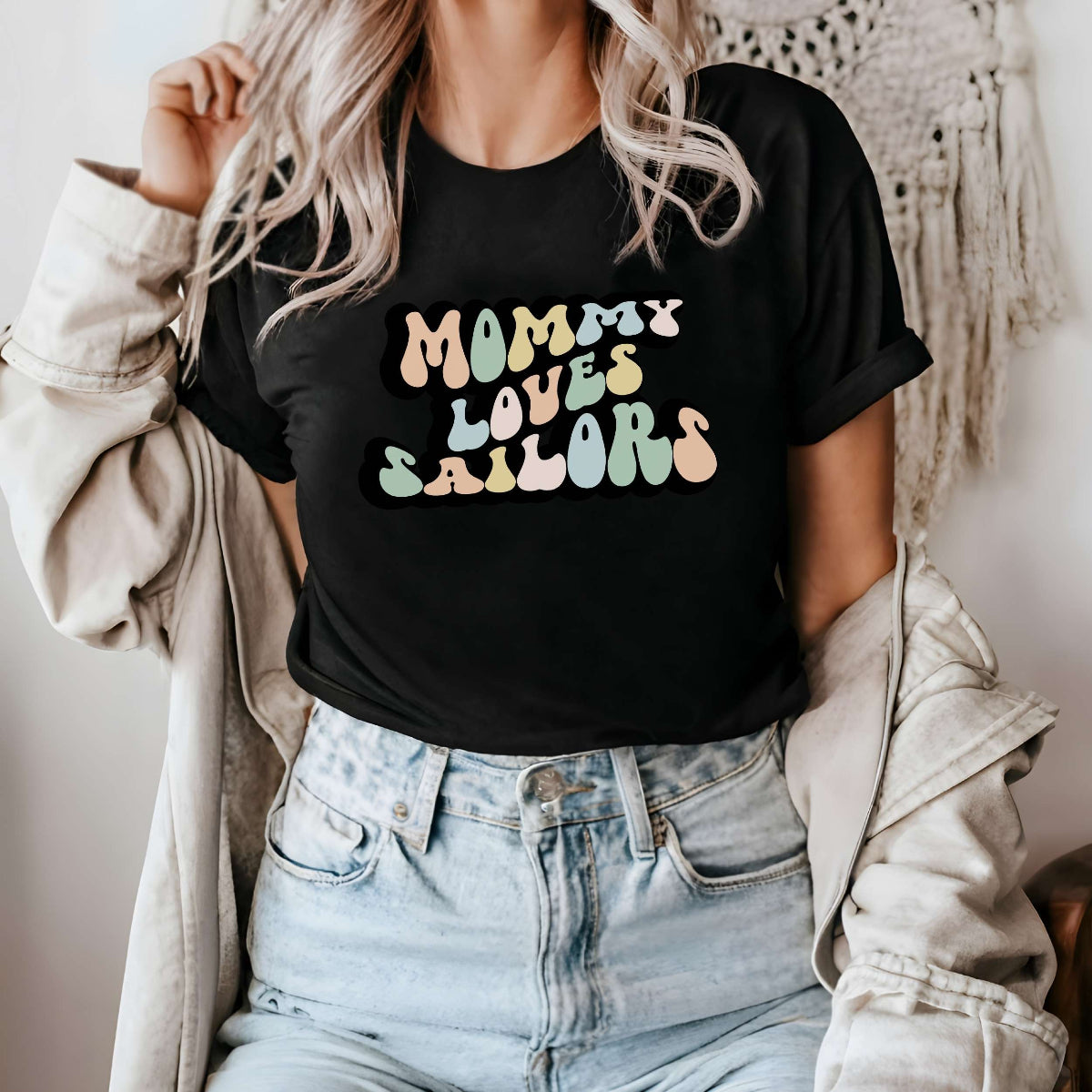 Graphic tee for women. The color of the shirt is black. In a colorful, typically 70s retro-style font it says Mommy Loves Sailors.