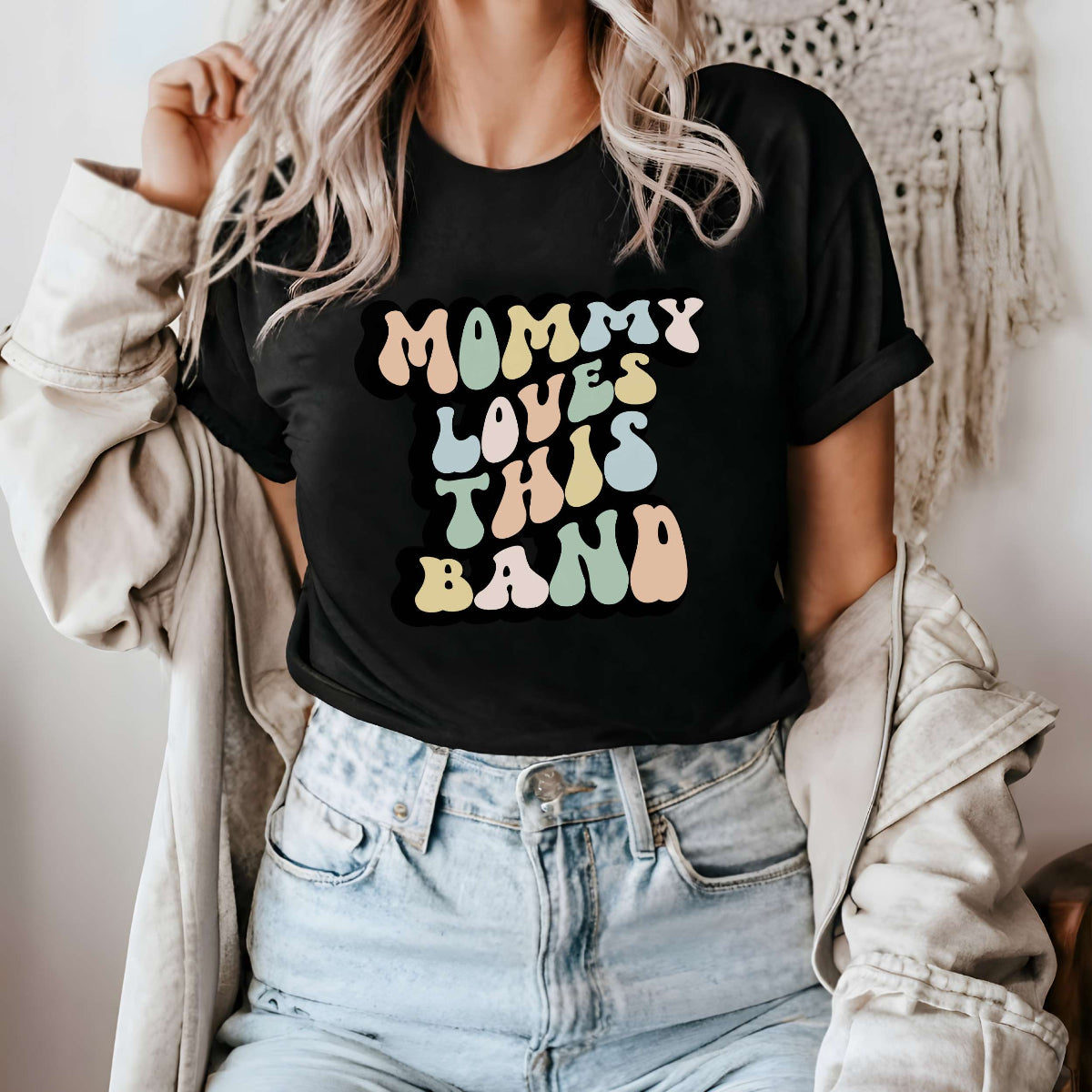 Graphic tee for women. The color of the shirt is black. In a colorful, typically 70s retro-style font it says Mommy Loves This Band.