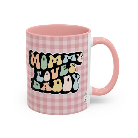 Perfect gift for mom. A decorative, 11oz ceramic mug. It’s wrapped in a soft pink-white checkered background. In a happy and colorful 70s retro-style font it says Mommy Loves Daddy, on both sides.