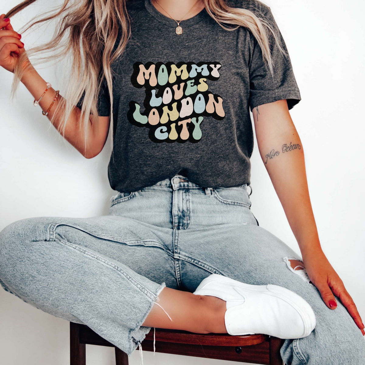 Graphic tee for women. The color of the shirt is gray heather. In a colorful, typically 70s retro-style font it says Mommy Loves London City.