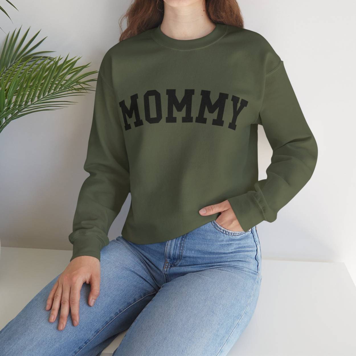 The perfect gift for mom. Our Mother’s Day special. Our crewneck sweatshirt. The color of the shirt is military green, and in big black varsity letters it says MOMMY on the chest. It’s available in six sizes, ranging from S to 3XL.