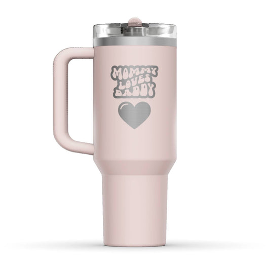 The back side of the newest Stanley 40oz Tumbler. The perfect gift for mom. The Color of the cup is Rose Quartz, a shade of soft pink. It’s engraved with a typically 70s retro-style font, saying Mommy Loves Daddy. Under that text there is a nice big heart in the same retro style.