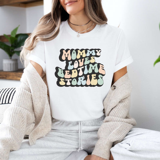 Graphic tee for women. The color of the shirt is white. In a colorful, typically 70s retro-style font it says Mommy Loves Bedtime Stories.