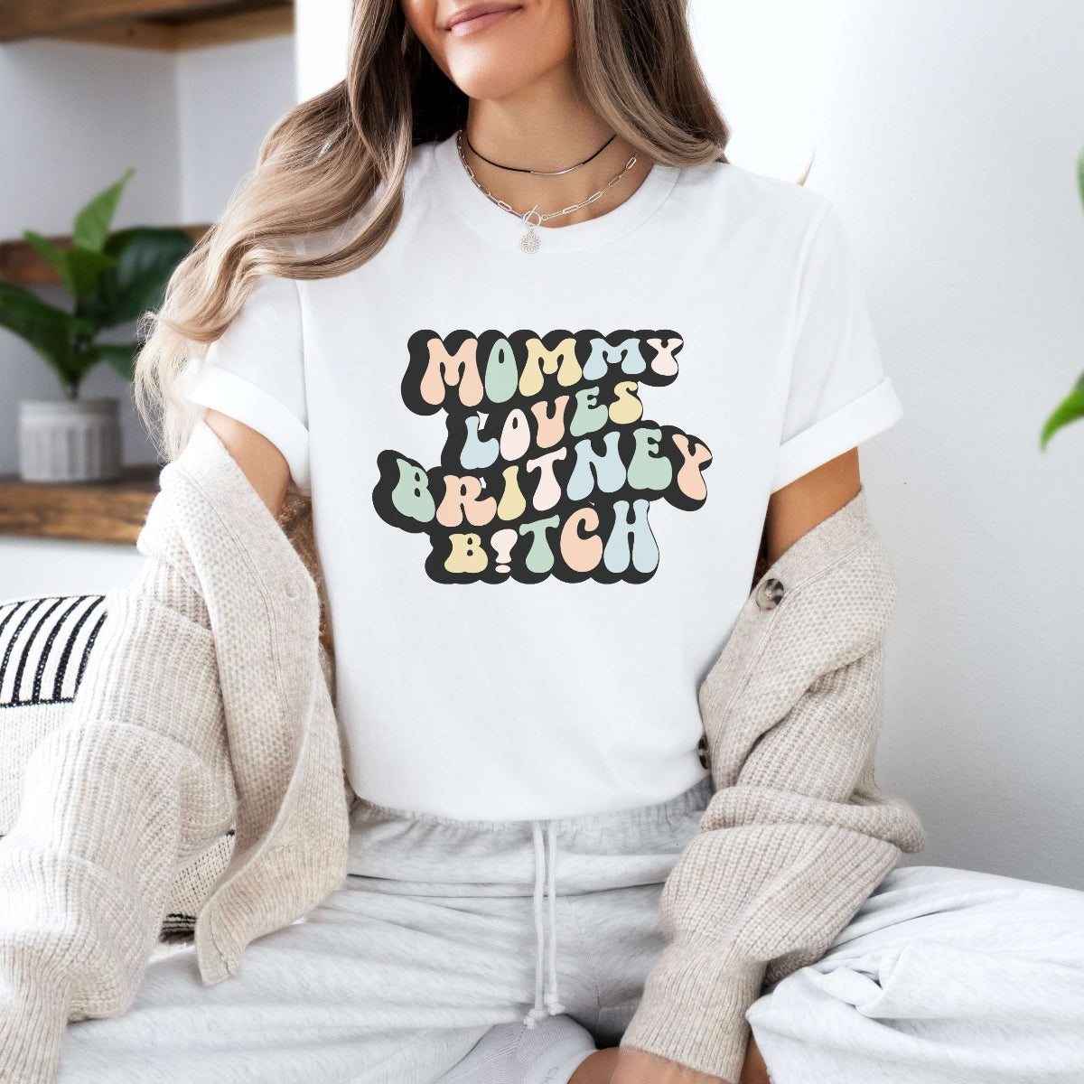 Graphic tee for women. The color of the shirt is white. In a colorful, typically 70s retro-style font it says Mommy Loves Britney B*tch.