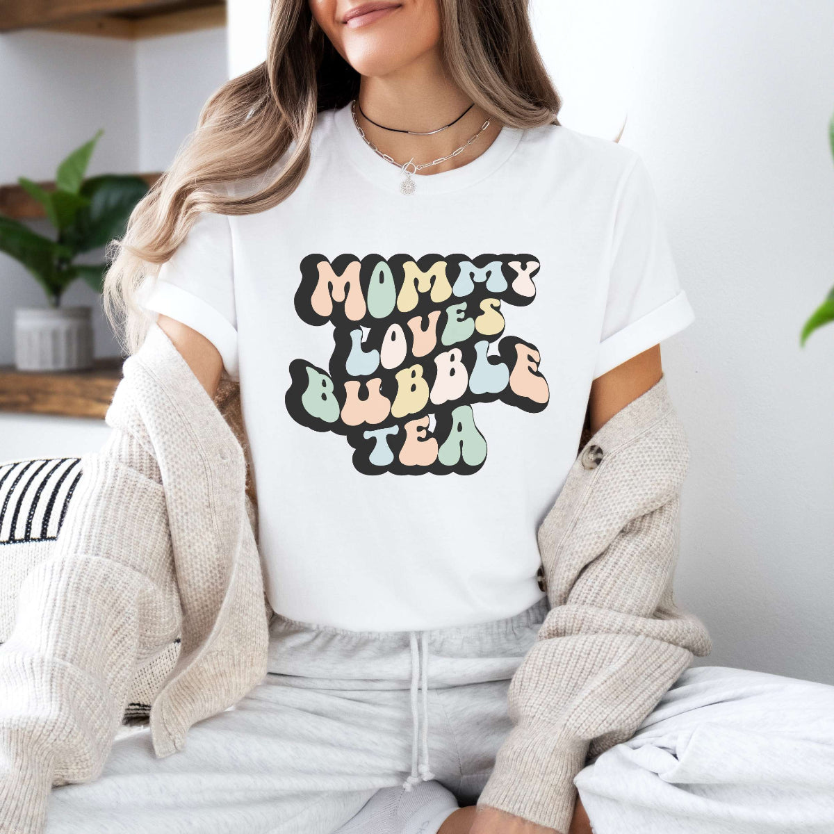 Graphic tee for women. The color of the shirt is white. In a colorful, typically 70s retro-style font it says Mommy Loves Bubble Tea.