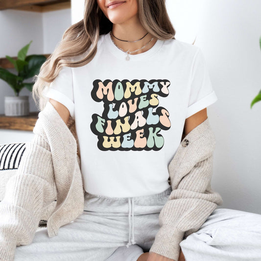 Graphic tee for women. The color of the shirt is white. In a colorful, typically 70s retro-style font it says Mommy Loves Finals Week.