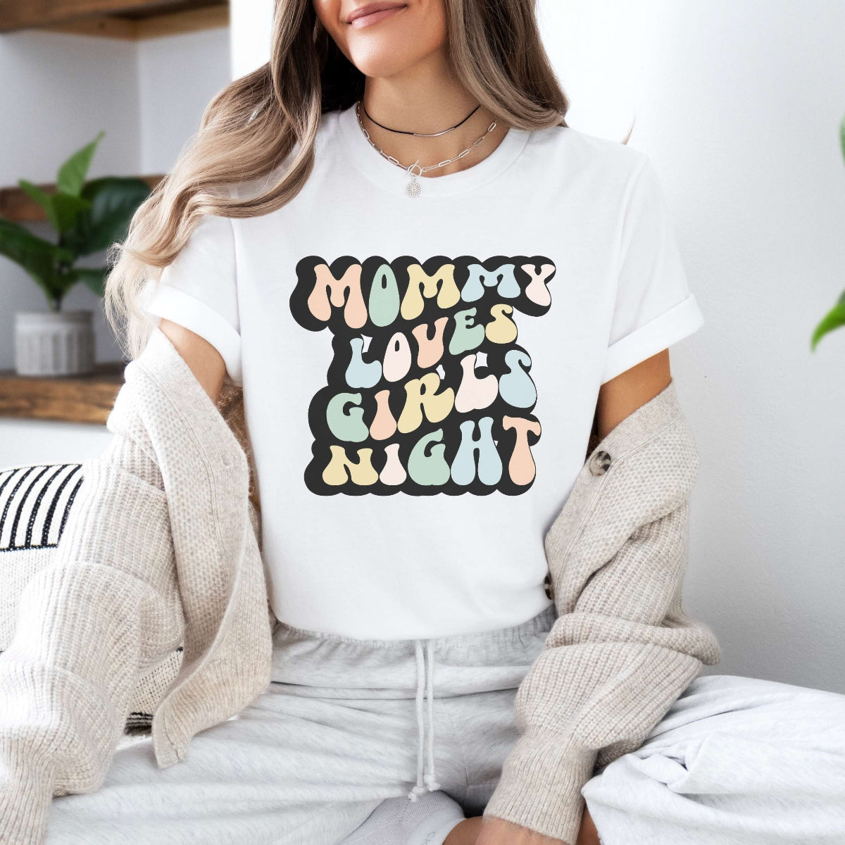 Graphic tee for women. The color of the shirt is white. In a colorful, typically 70s retro-style font it says Mommy Loves Girls Night.