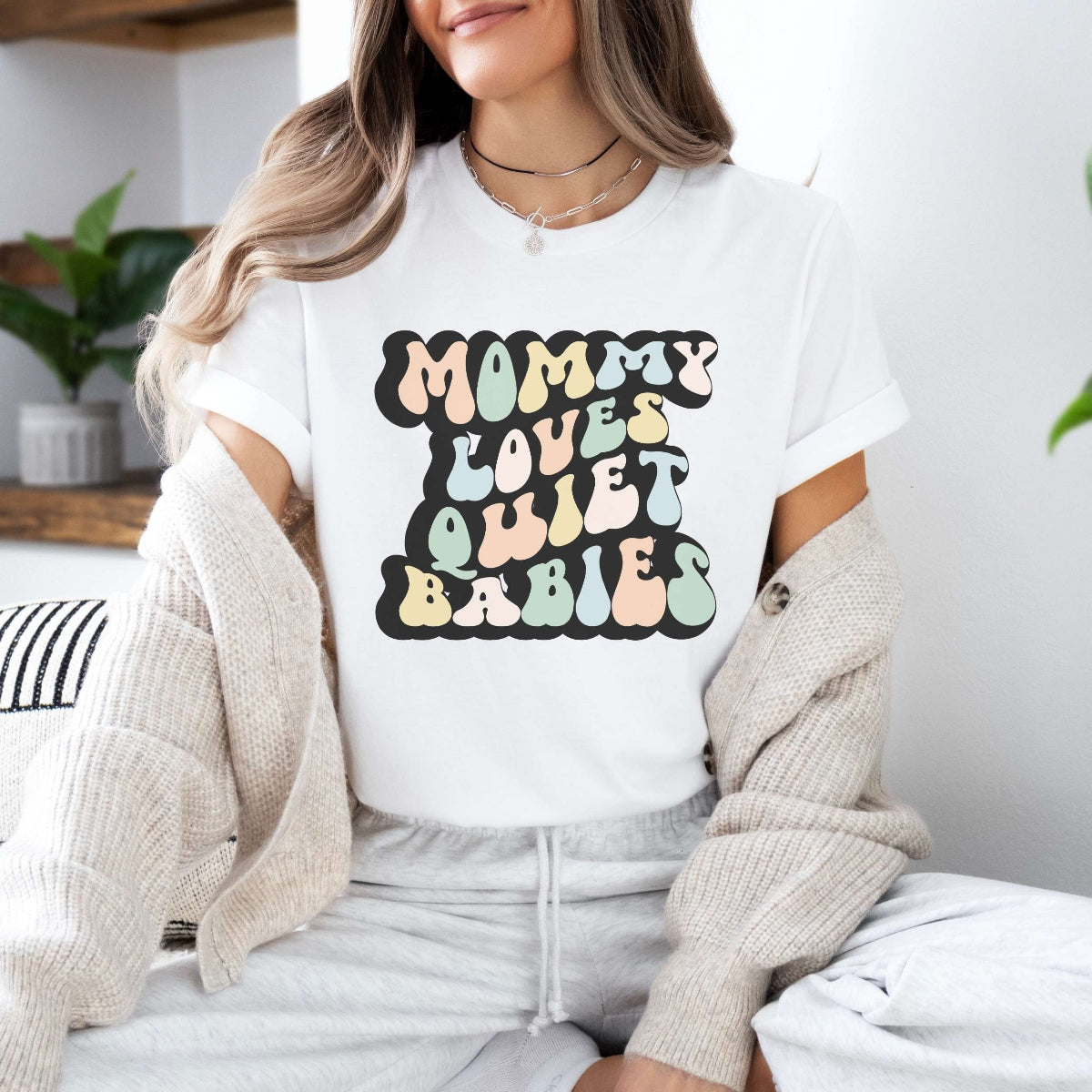 Graphic tee for women. The color of the shirt is white. In a colorful, typically 70s retro-style font it says Mommy Loves Quiet Babies.