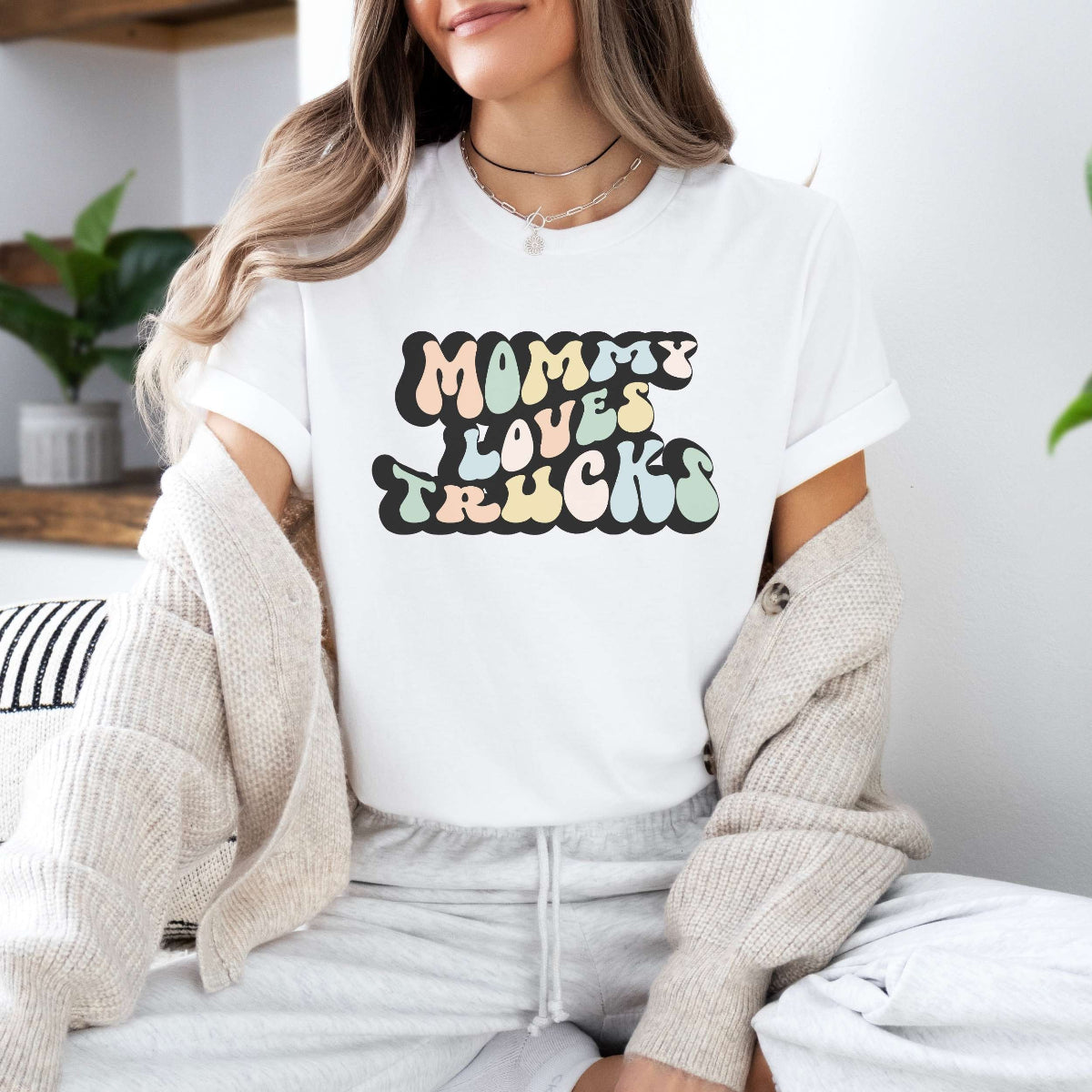 Graphic tee for women. The color of the shirt is white. In a colorful, typically 70s retro-style font it says Mommy Loves Trucks.
