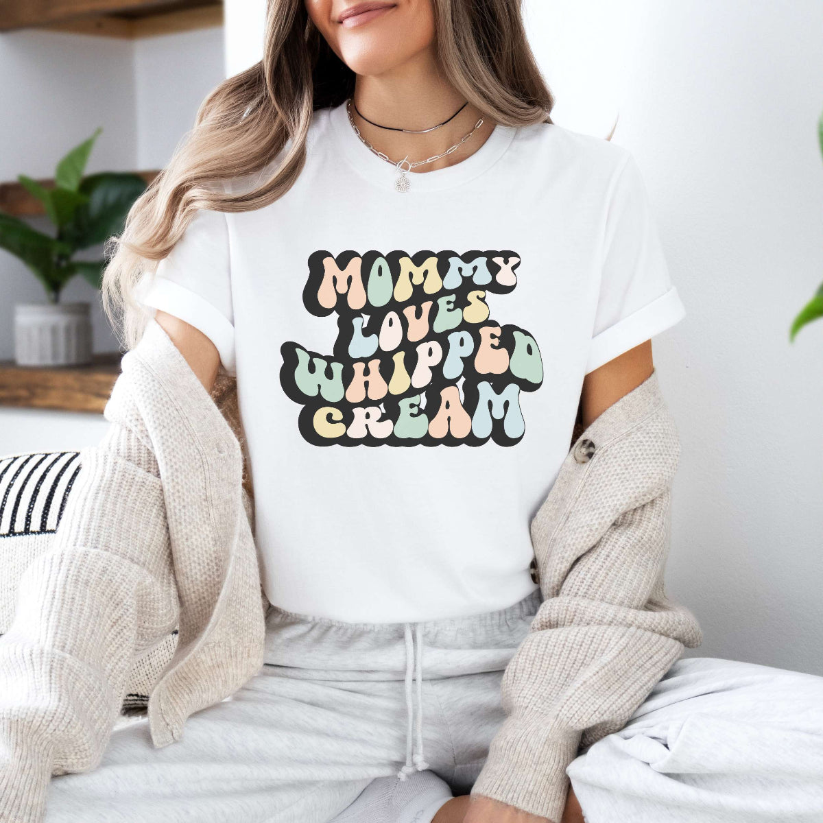 Graphic tee for women. The color of the shirt is white. In a colorful, typically 70s retro-style font it says Mommy Loves Whipped Cream.