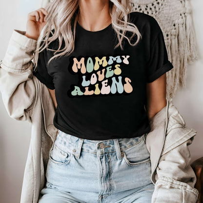 Graphic tee for women. The color of the shirt is black. In a colorful, typically 70s retro-style font it says Mommy Loves Aliens.