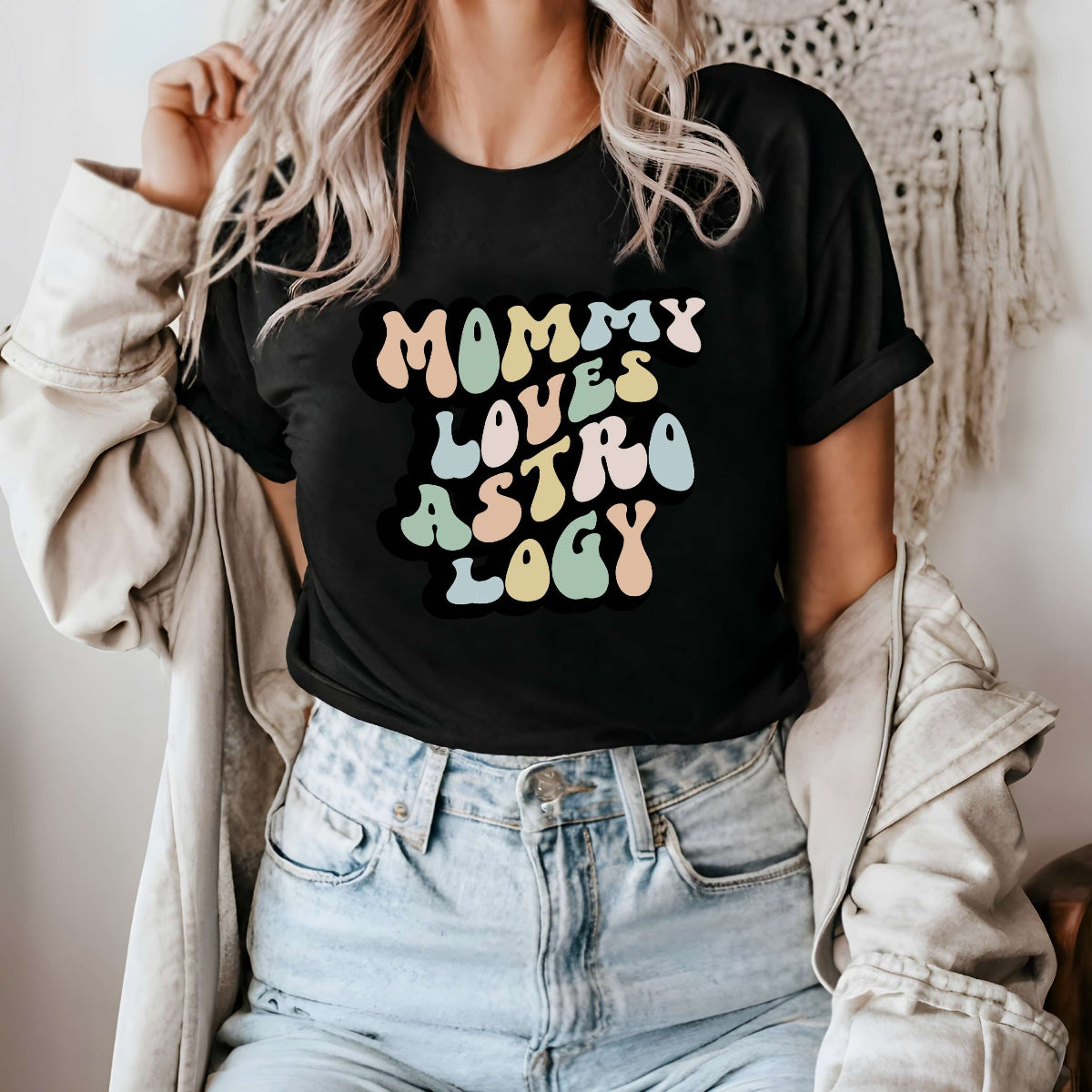 Graphic tee for women. The color of the shirt is black. In a colorful, typically 70s retro-style font it says Mommy Loves Astrology.
