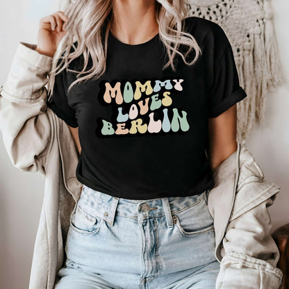 Graphic tee for women. The color of the shirt is black. In a colorful, typically 70s retro-style font it says Mommy Loves Berlin.