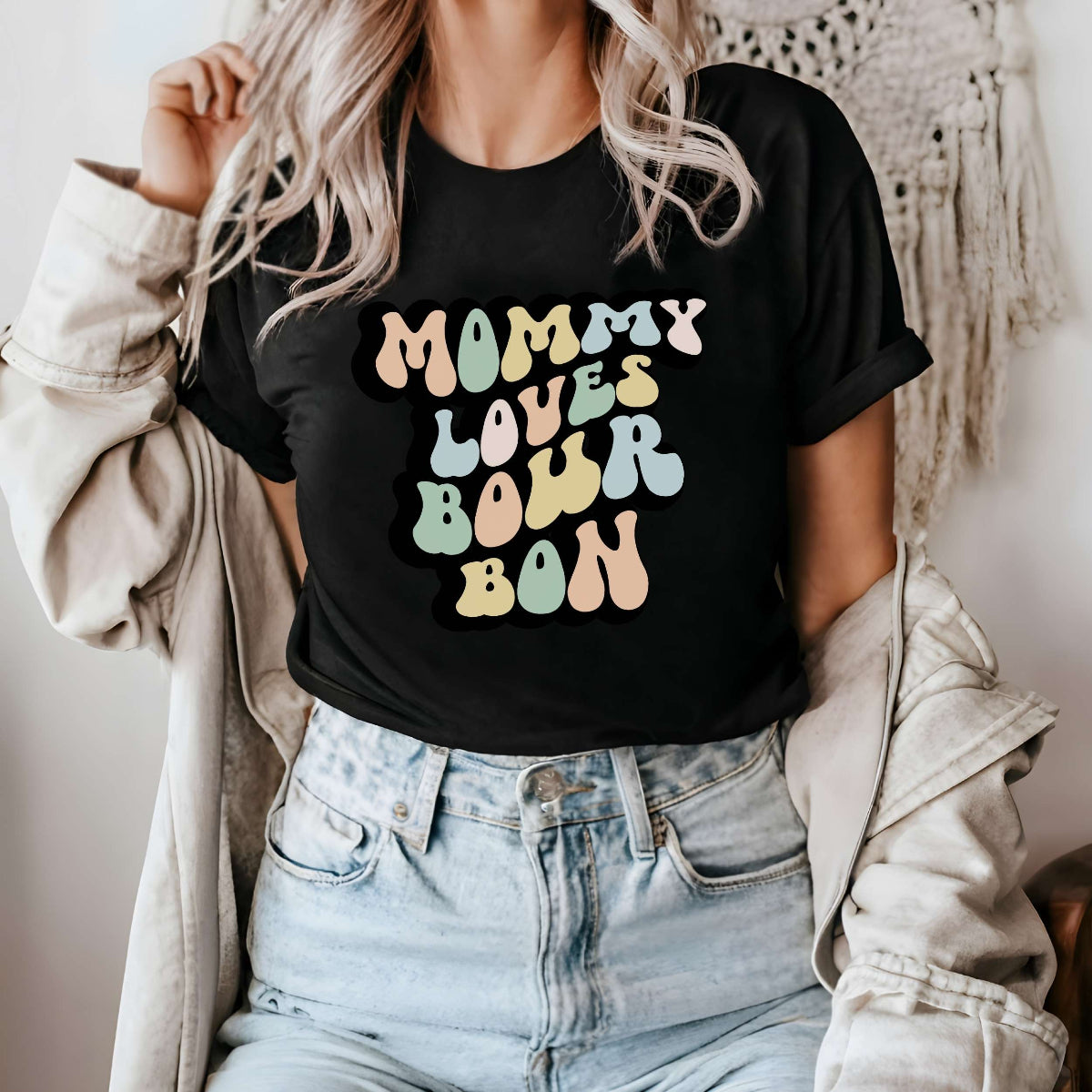 Graphic tee for women. The color of the shirt is black. In a colorful, typically 70s retro-style font it says Mommy Loves Bourbon.