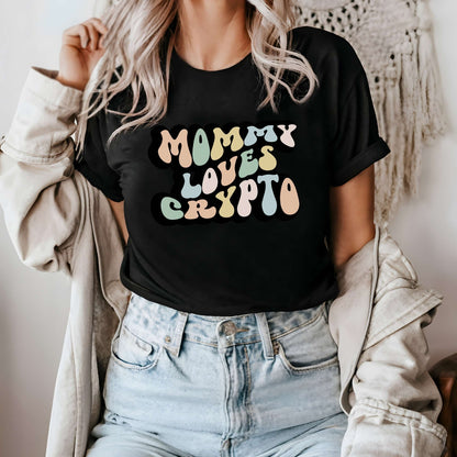 Graphic tee for women. The color of the shirt is black. In a colorful, typically 70s retro-style font it says Mommy Loves Crypto.