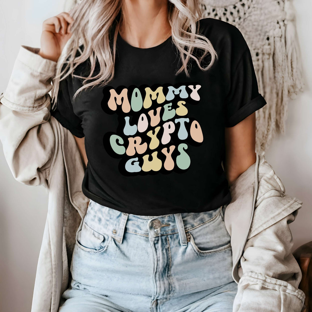 Graphic tee for women. The color of the shirt is black. In a colorful, typically 70s retro-style font it says Mommy Loves Crypto Guys.