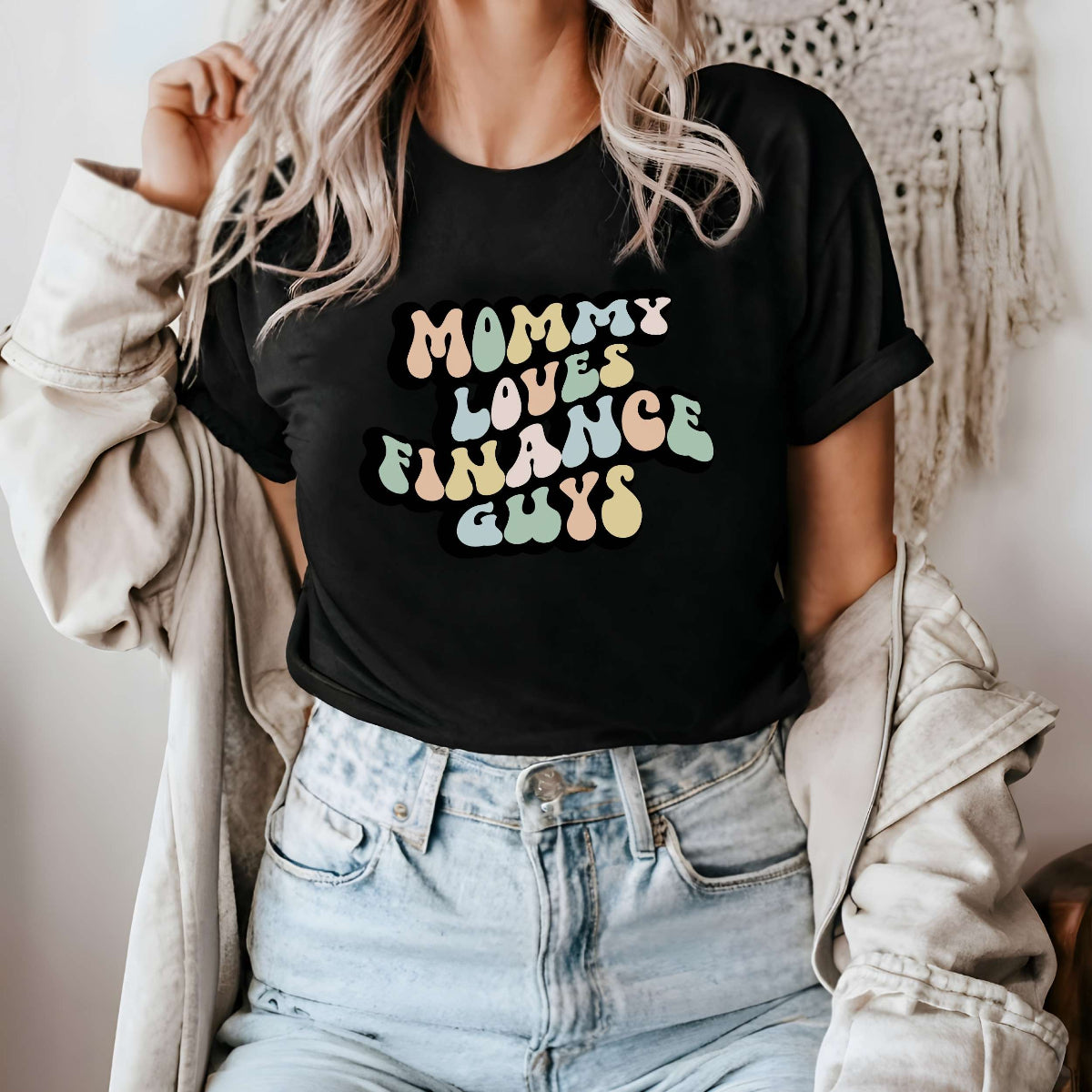 Graphic tee for women. The color of the shirt is black. In a colorful, typically 70s retro-style font it says Mommy Loves Finance Guys.
