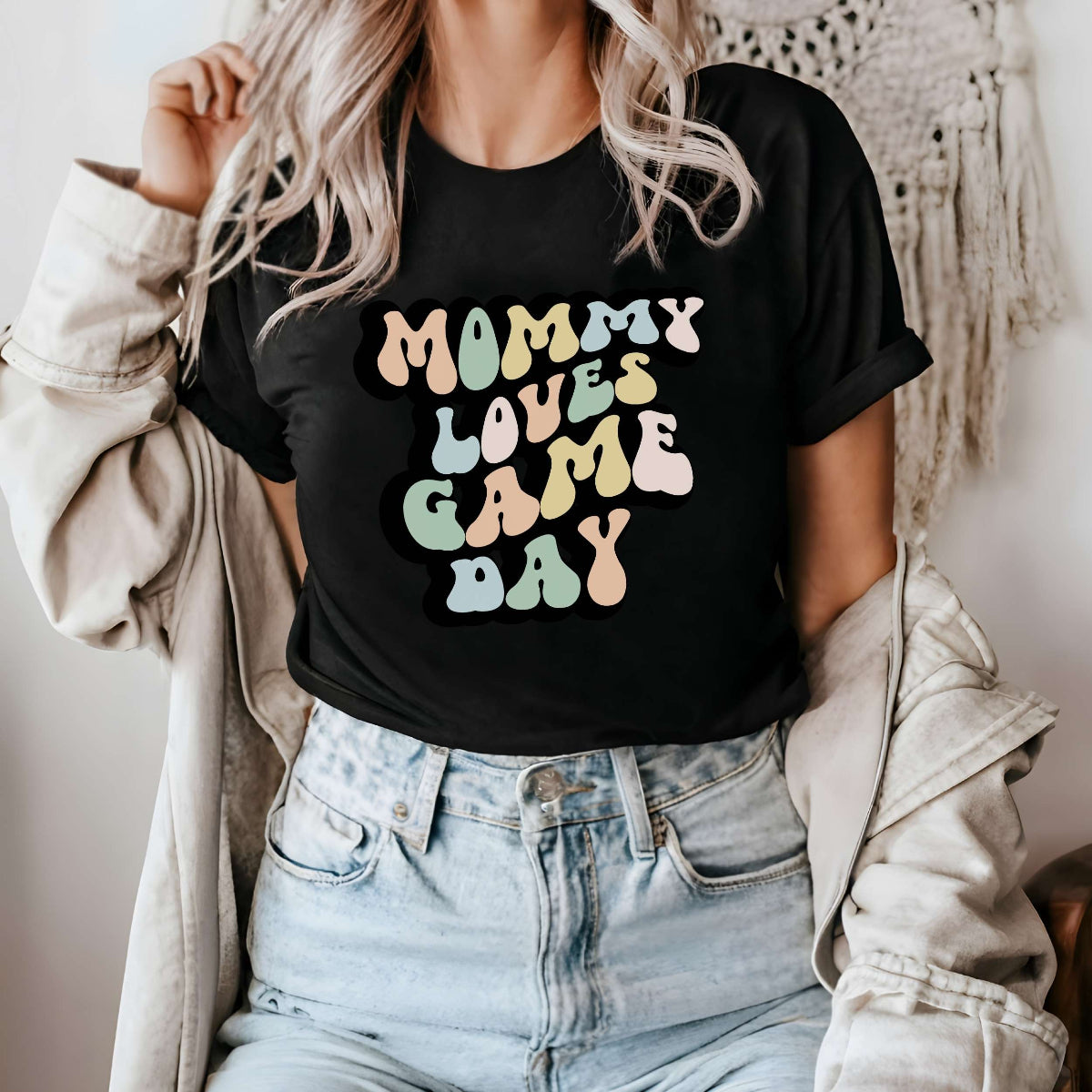 Graphic tee for women. The color of the shirt is black. In a colorful, typically 70s retro-style font it says Mommy Loves Game Day.