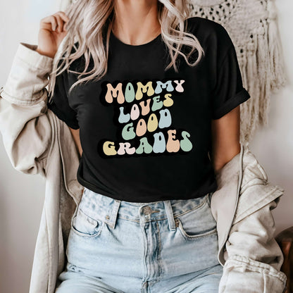 Graphic tee for women. The color of the shirt is black. In a colorful, typically 70s retro-style font it says Mommy Loves Good Grades.