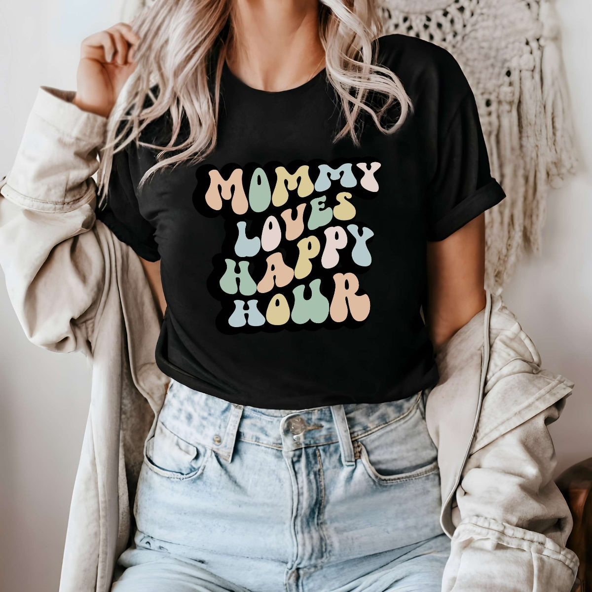 Graphic tee for women. The color of the shirt is black. In a colorful, typically 70s retro-style font it says Mommy Loves Happy Hour.