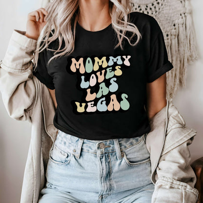 Graphic tee for women. The color of the shirt is black. In a colorful, typically 70s retro-style font it says Mommy Loves Las Vegas.