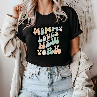 Graphic tee for women. The color of the shirt is black. In a colorful, typically 70s retro-style font it says Mommy Loves New York.