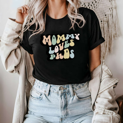 Graphic tee for women. The color of the shirt is black. In a colorful, typically 70s retro-style font it says Mommy Loves PhDs.