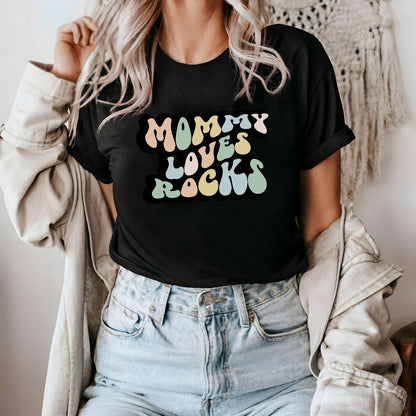 Graphic tee for women. The color of the shirt is black. In a colorful, typically 70s retro-style font it says Mommy Loves Rocks.