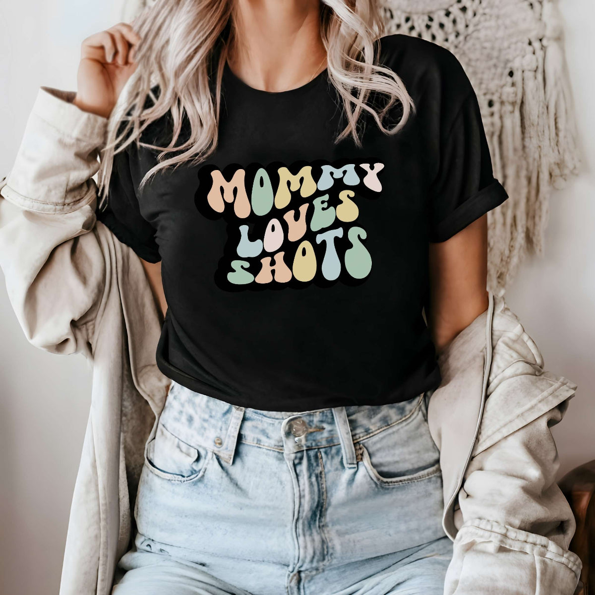 Graphic tee for women. The color of the shirt is black. In a colorful, typically 70s retro-style font it says Mommy Loves Shots.