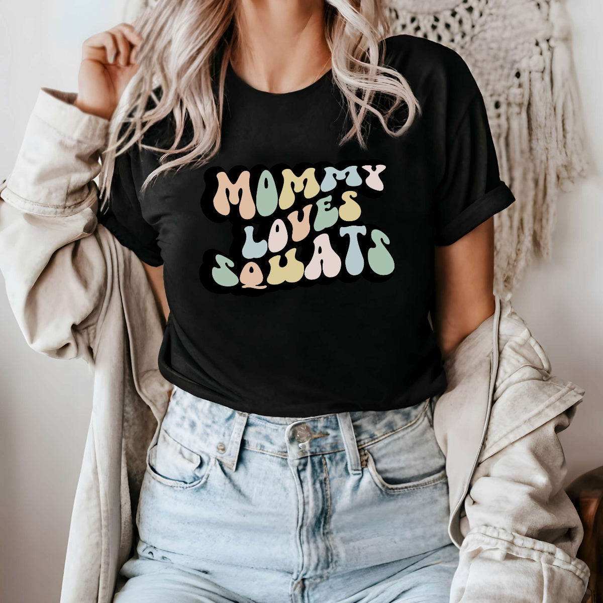 Graphic tee for women. The color of the shirt is black. In a colorful, typically 70s retro-style font it says Mommy Loves Squats.