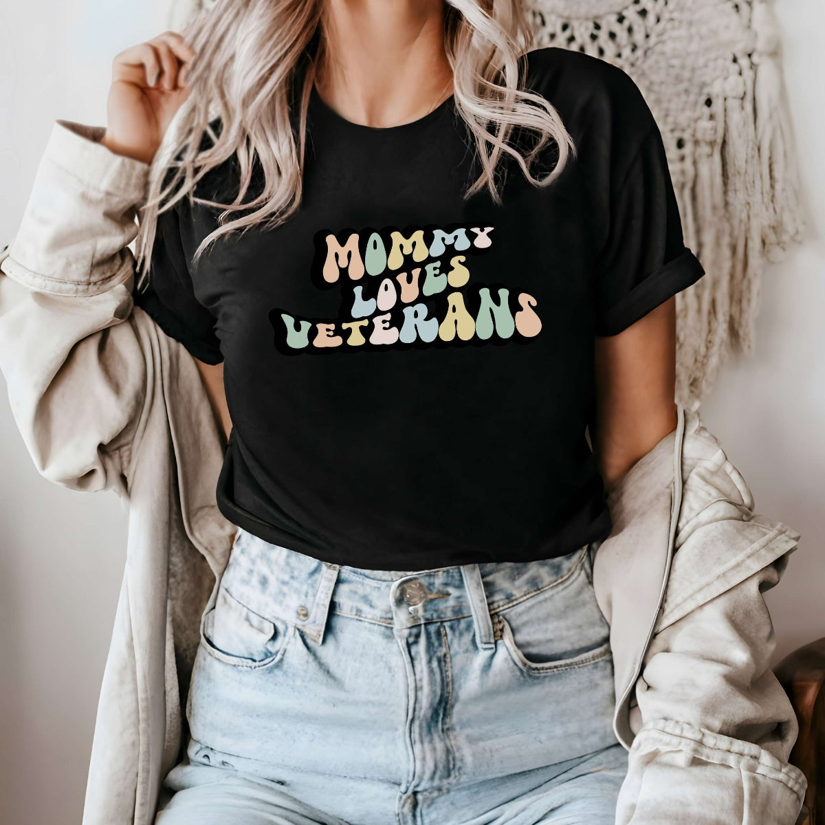 Graphic tee for women. The color of the shirt is black. In a colorful, typically 70s retro-style font it says Mommy Loves Veterans.