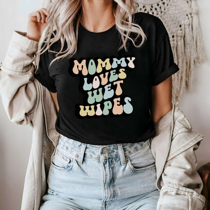 Graphic tee for women. The color of the shirt is black. In a colorful, typically 70s retro-style font it says Mommy Loves Wet Wipes.