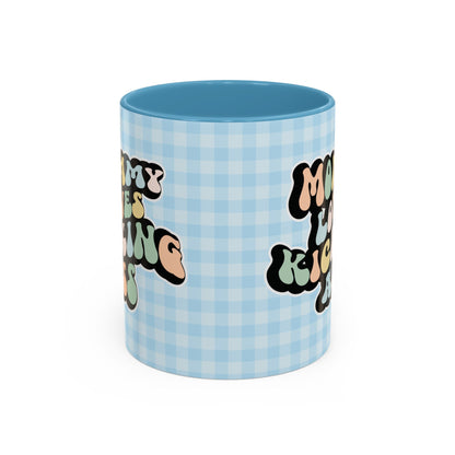 Perfect gift for mom. A decorative, 11oz ceramic mug. It’s wrapped in a light blue-white checkered background. In a happy and colorful 70s retro-style font it says Mommy Loves Kicking Ass on both sides. 