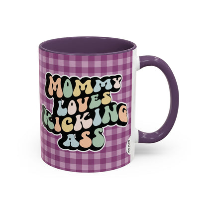 Perfect gift for mom. A decorative, 11oz ceramic mug. It’s wrapped in a purple-white checkered background. In a happy and colorful 70s retro-style font it says Mommy Loves Kicking Ass on both sides. 