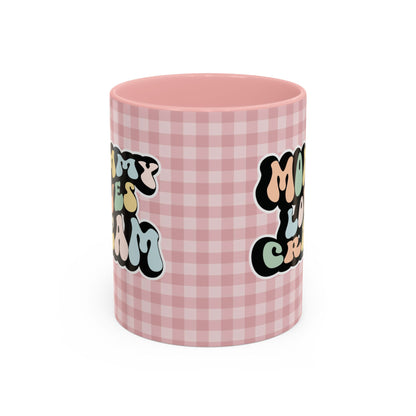 Perfect gift for mom. A decorative, 11oz ceramic mug. It’s wrapped in a soft pink-white checkered background. In a happy and colorful 70s retro-style font it says Mommy Loves Cream, on both sides. 