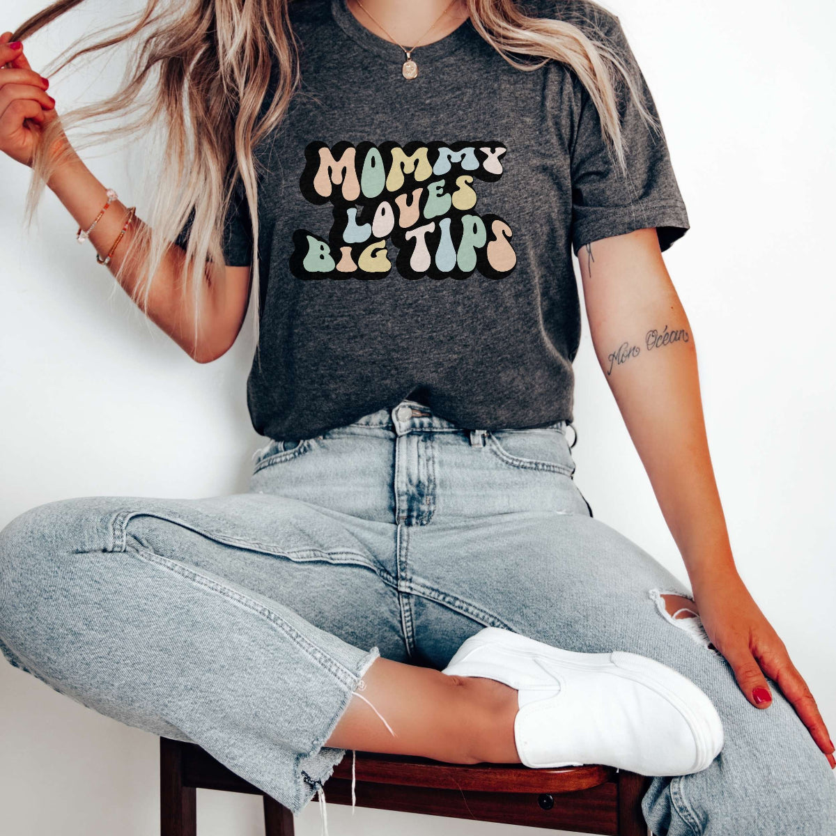Graphic tee for women. The color of the shirt is gray heather. In a colorful, typically 70s retro-style font it says Mommy Loves Big Tips.