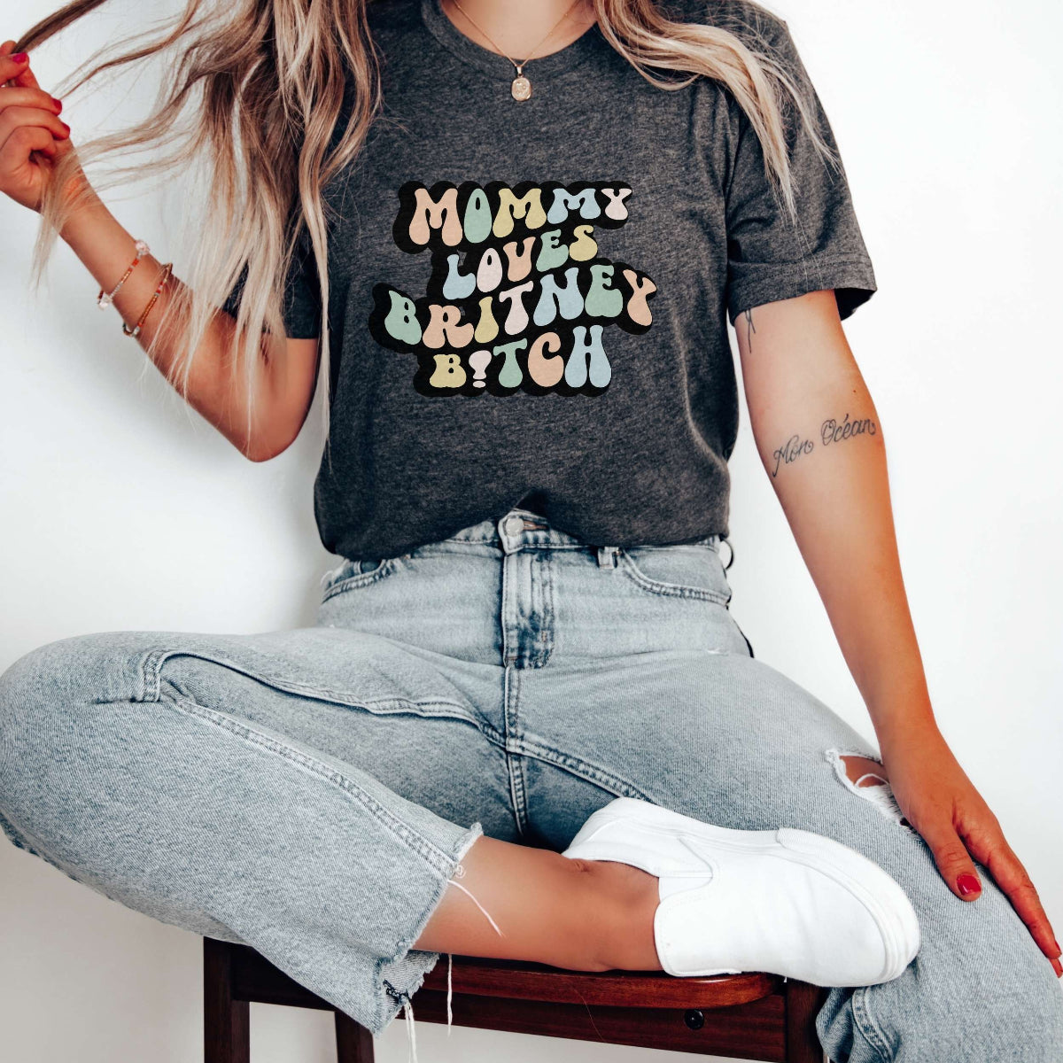 Graphic tee for women. The color of the shirt is gray heather. In a colorful, typically 70s retro-style font it says Mommy Loves Britney B*tch.